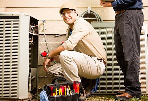 Two men performing emergency repairs on an air conditioner in a residential setting.
