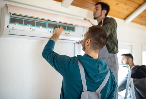 wo men installing an air conditioner in a garage, focused on their work and collaborating on the installation process.