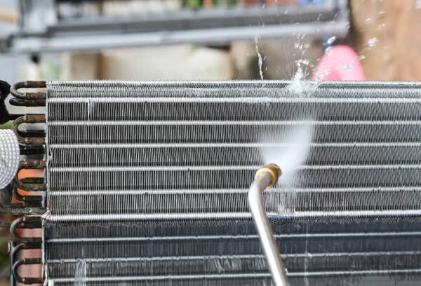 A man uses a hose to clean a radiator, focusing on AC coil cleaning for improved efficiency.
