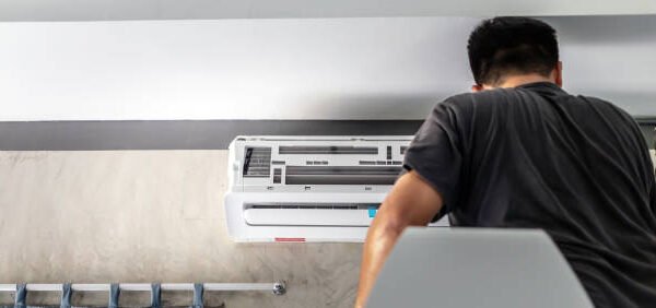 A man is working on fixing an air conditioner inside a room, demonstrating AC installation techniques.