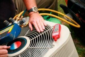 A close-up of a technician's hand and professional testing equipment on top of an AC condenser unit during Regular hvac maintenance plan