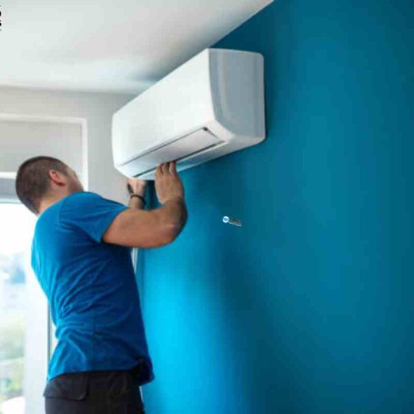 A man repairs wall AC units in a room, focused on the unit with tools nearby on a table, illustrating hands-on maintenance in a residential setting.