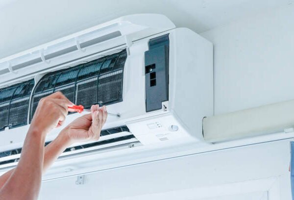 Technician performing Central AC Service, repairing an air conditioner with tools focused on the unit’s internal components.