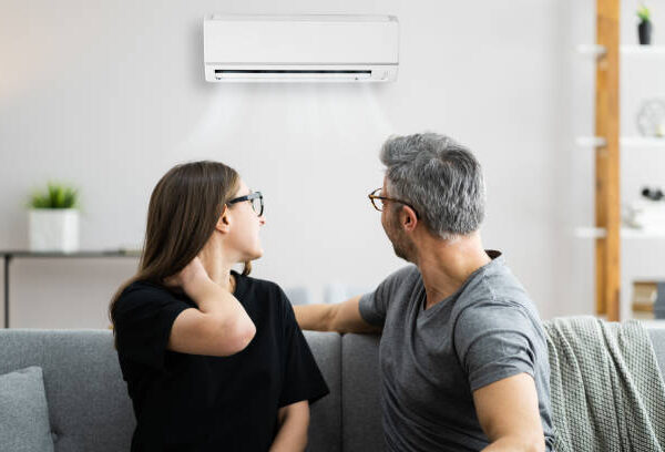  man and woman relax on a couch, with an air conditioner running nearby, but it is not providing cool air.