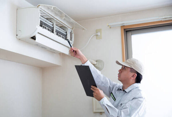 A man in a white shirt and hat holds a clipboard, assessing an air conditioning unit labeled "AC Running but Not Cooling."