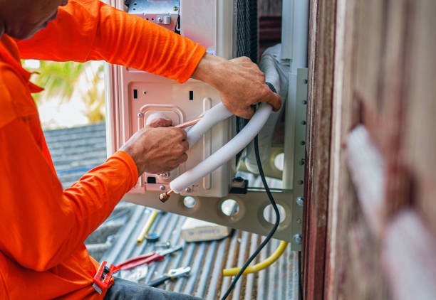 A man in an orange shirt repairs a water heater during an emergency AC repair situation.