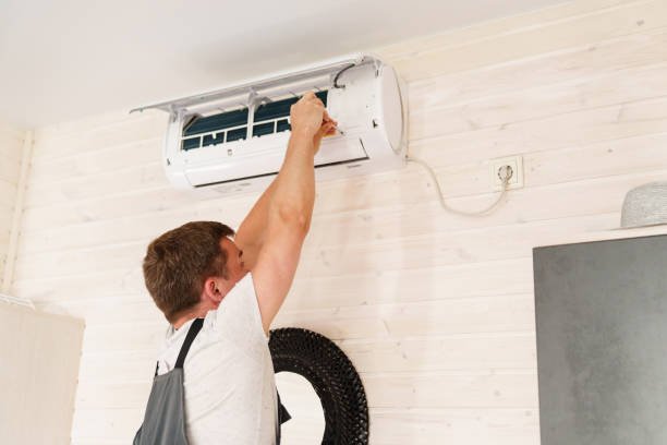 A man adjusting an air conditioning unit in a room, demonstrating AC installation skills.