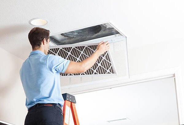 "An HVAC technician changing a home ceiling air filter as part of a routine checklist for Regular HVAC Maintenance.
