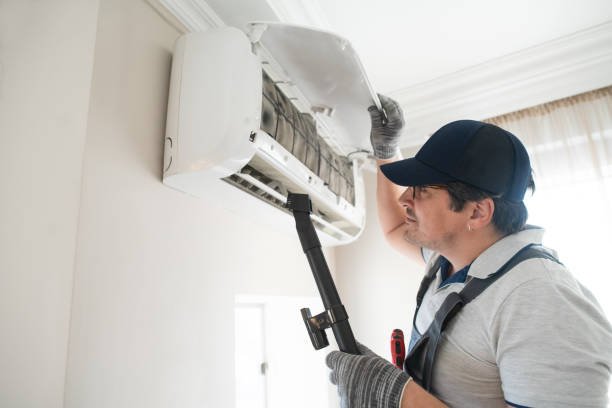 A man in a hat and overalls repairs an air conditioner that ac not turning on.