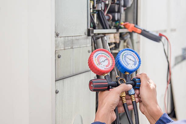 A person holds two pressure gauges against a wall, related to AC refrigerant leak services.