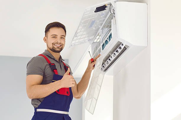 A man in overalls and an apron holds a white air conditioner, promoting Air Flow Improvement Services.