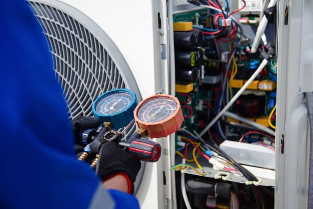A technician in blue overalls checks an air conditioner gauge, representing emergency AC services.