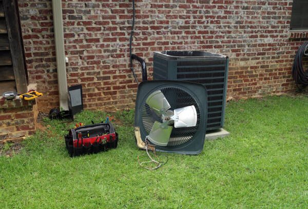 A large air conditioner and a fan placed on the grass, showcasing an air handler setup in an outdoor environment.
