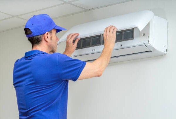 A man in a blue shirt diagnosing and fixing an air conditioner unit.
