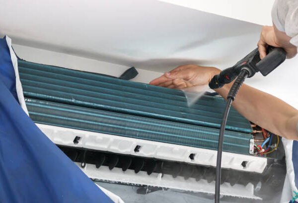 A man is cleaning an air conditioner with a hose, highlighting the importance of HVAC inspection services. 