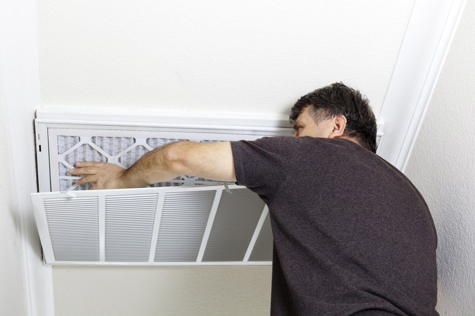 A man repairs an air conditioner in a room, focusing on improving air flow for better comfort.