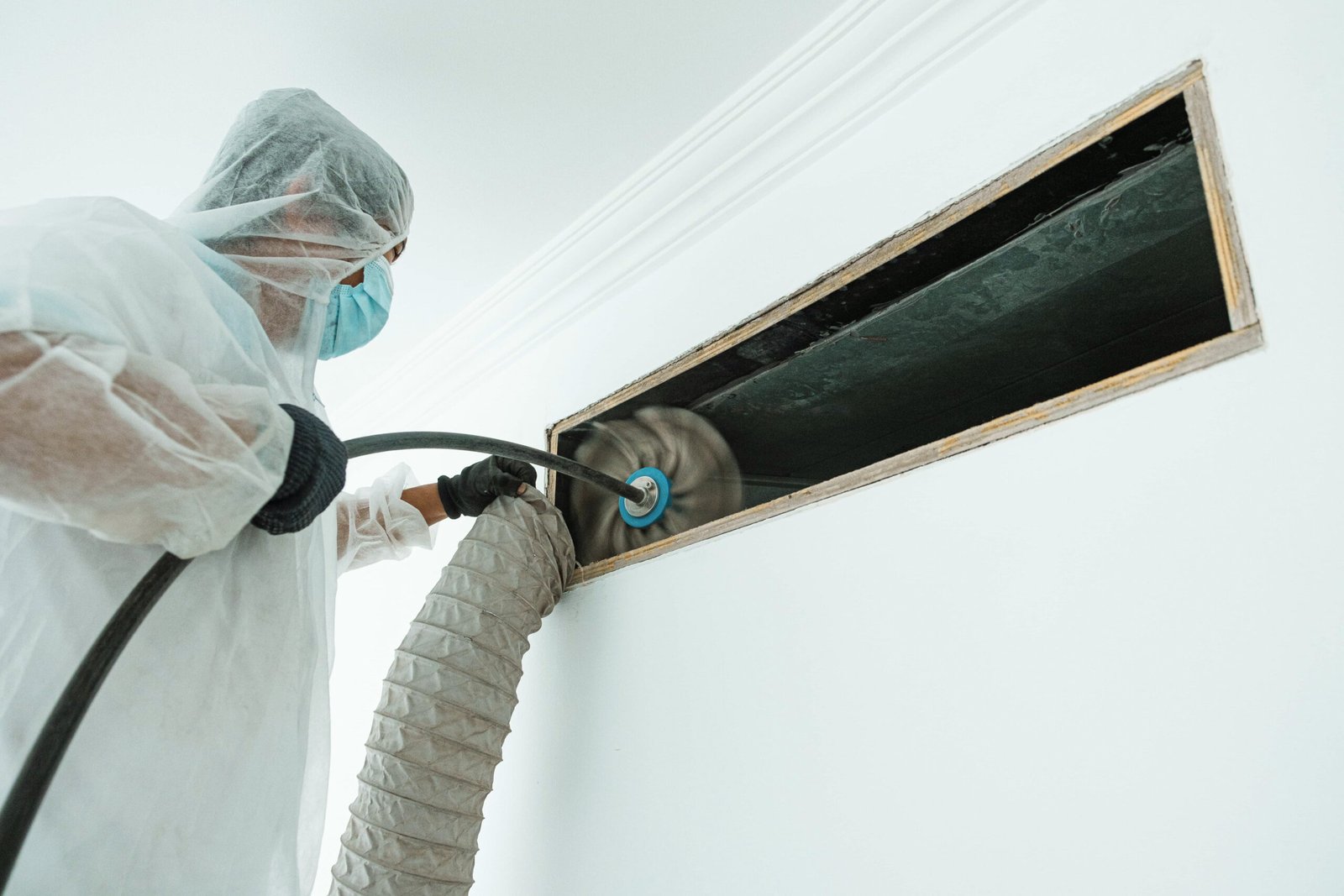 A man in a white coat and mask cleans a window, part of a duct cleaning service.