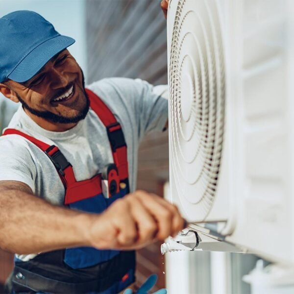 A man in overalls and a hat repairs an air conditioner for an HVAC company.