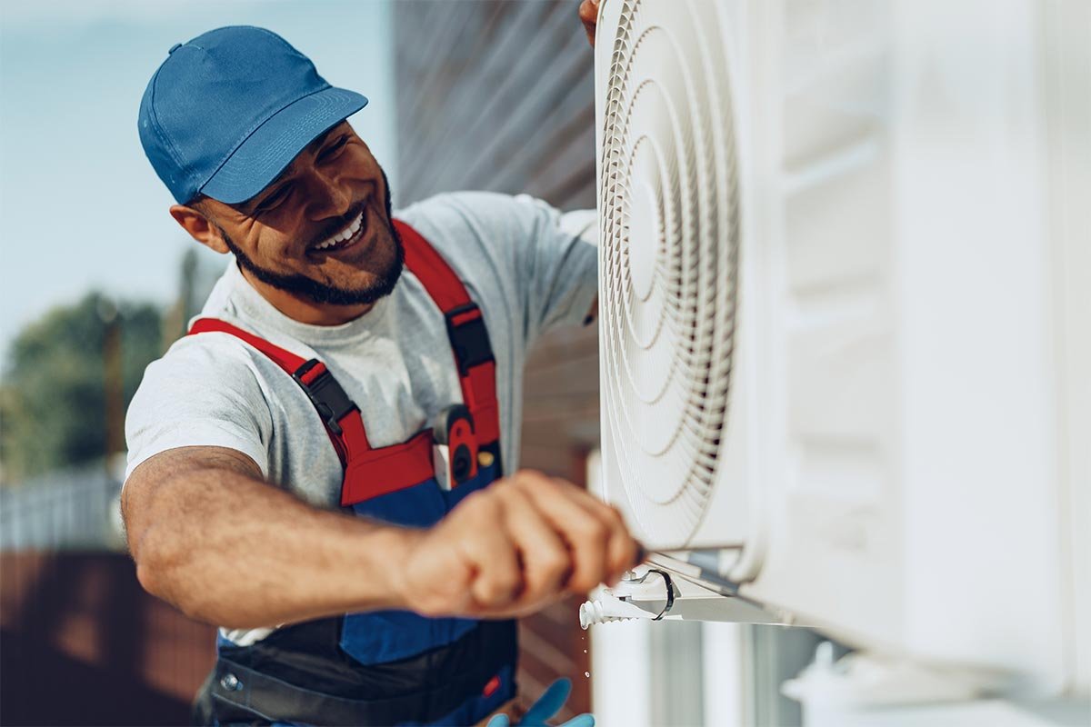 A man in overalls and a hat repairs an air conditioner for a hvac maintenance plan