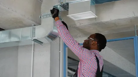 Technician wearing a hard hat mounting ceiling ventilation ductwork as part of a commercial Duct Installation process