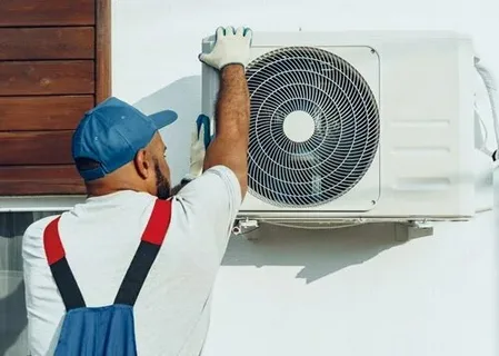 HVAC installation in progress on a residential rooftop with an installer utilizing manifold gauges and a blue vacuum pump tank